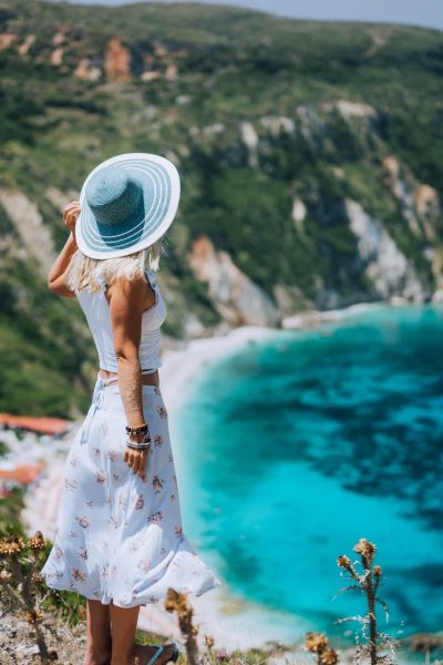 Young woman on Petani beach Kefalonia, admiring highly excited picturesque panorama of emerald blue bay of Mediterranean sea and steep coastline hills. Greece.